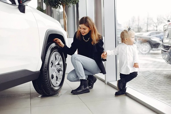 An image of a smiling woman with her daughter looking at a new car.