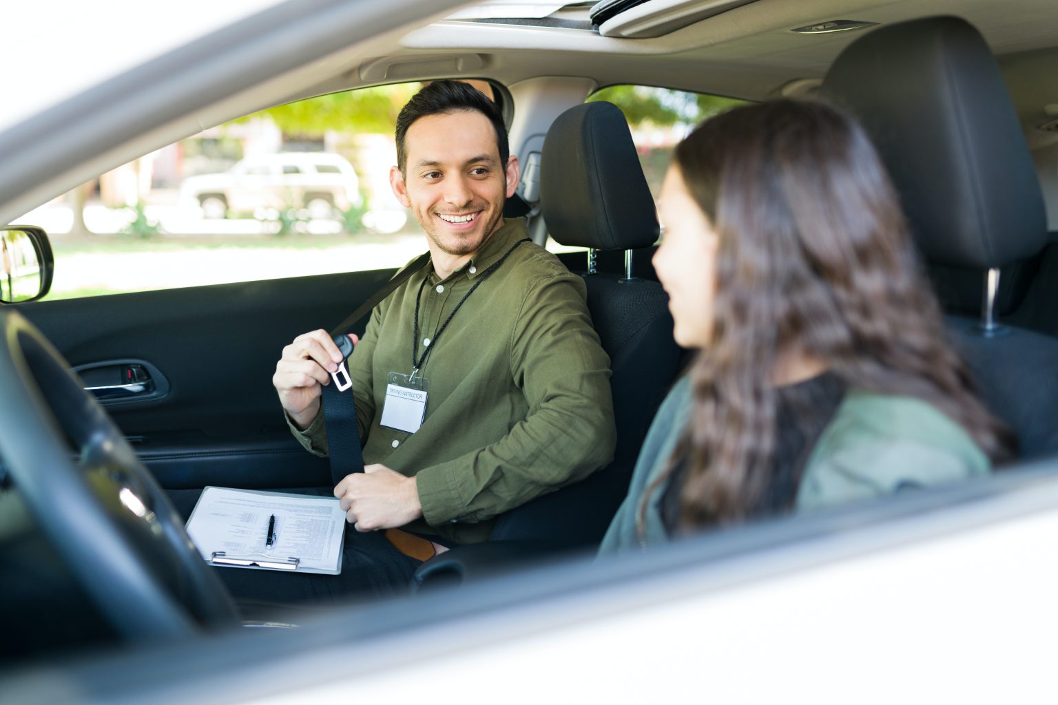 A male driving instructor, smiling and teaching a young girl to drive