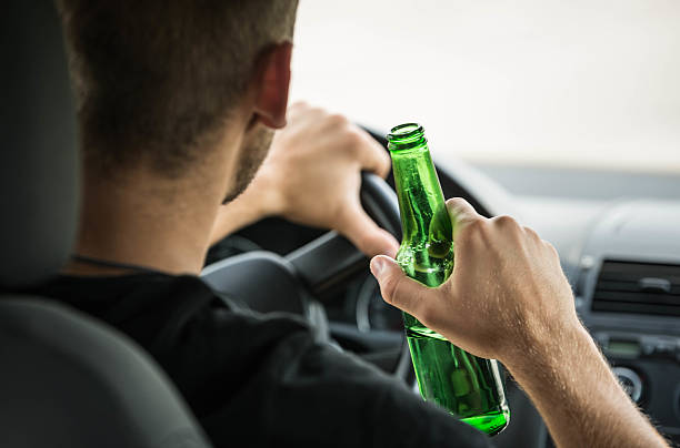 A man drinking a beer while driving a car under the influence of alcohol